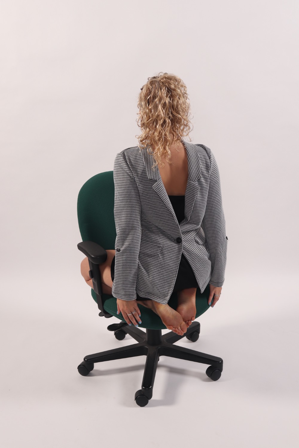 A woman kneeling backwards in an office chair on a white background. Her clothes are on backward too.